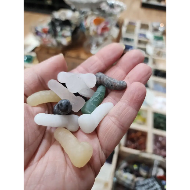 Assorted 1 inch penis-shaped crystal carvings in various colors and stones, hand-carved and displayed on a white background. Perfect for playful energy, empowerment, and root chakra healing.