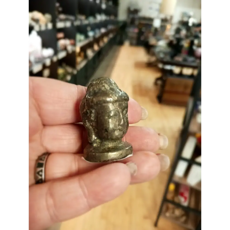 Hand-carved 1 1/2 inch tall Buddha head figurines in assorted crystal materials such as amethyst, rose quartz, clear quartz, and jade, displayed on a white background.
