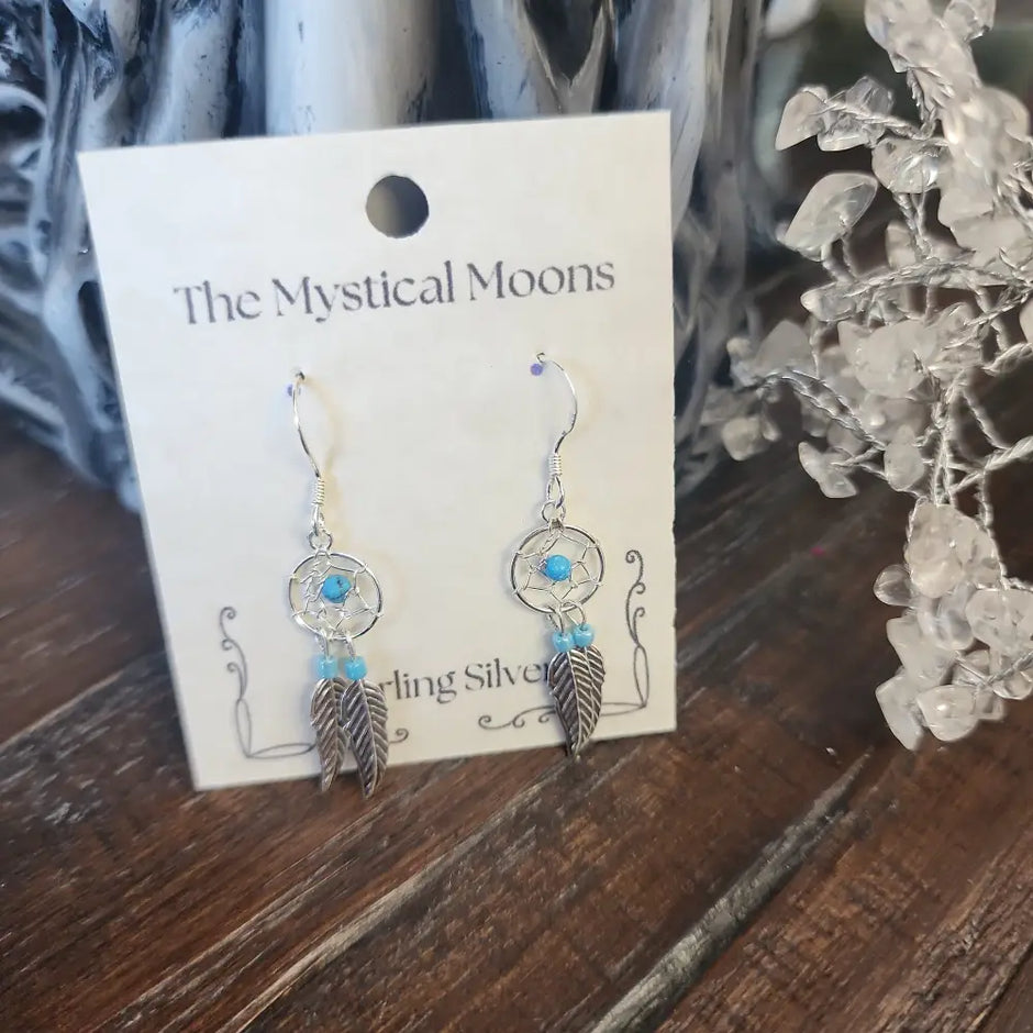 Sterling silver earrings featuring an intricate dreamcatcher with two feather charms, displayed on a white background. Perfect for protection, inspiration, and boho spirit.