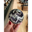 Hand-polished Dream Amethyst sphere featuring vivid purple and white chevron bands, displayed on a white background.