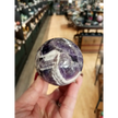 Hand-polished Dream Amethyst sphere featuring vivid purple and white chevron bands, displayed on a white background.