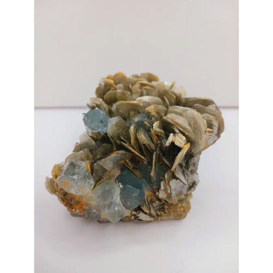 Muscovite with aquamarine specimen, showcasing shimmering layers and blue crystal accents, displayed on a white background.