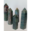 Hand-polished Green Zoisite stone featuring vibrant green hues, sometimes with black or ruby inclusions, displayed on a white background.