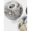 Quartz, garnet, tourmaline, and mica sphere, polished with clear, red, black, and shimmering inclusions, displayed on a white background.