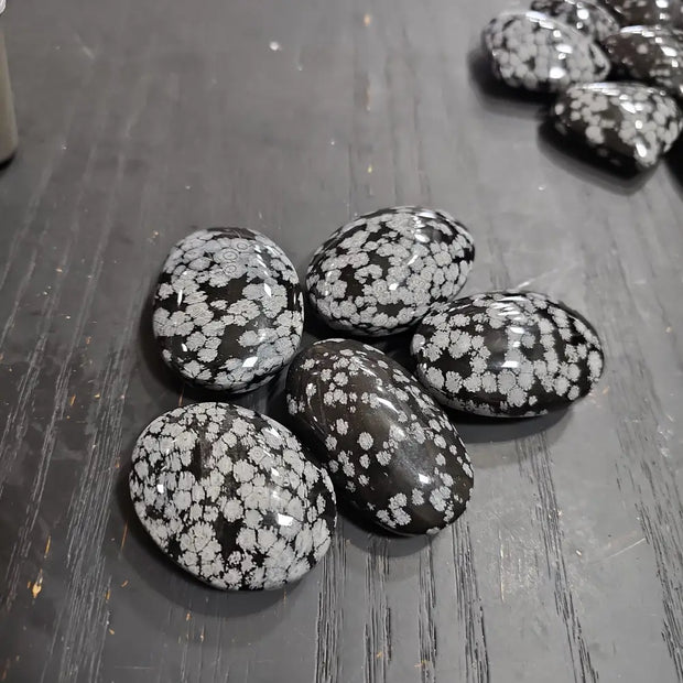 Hand-polished snowflake obsidian hearts and palmstones, featuring black stone with white snowflake patterns, displayed on a white background. Perfect for grounding, protection, and gentle transformation.